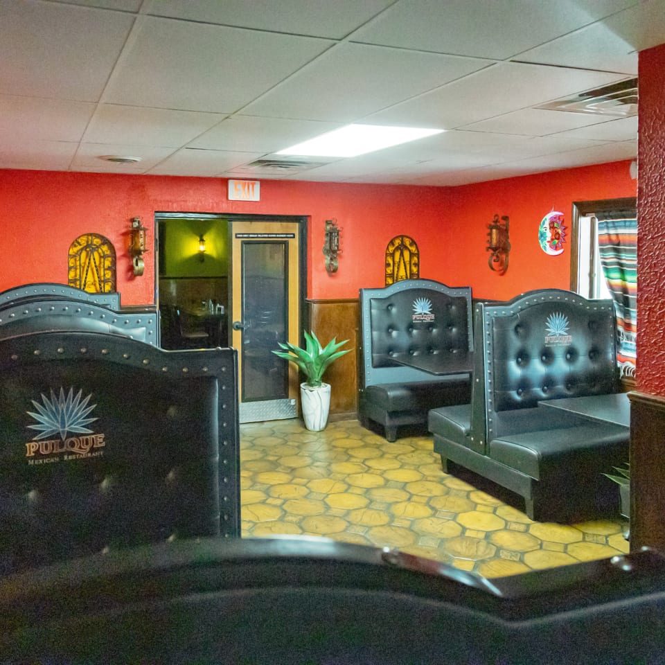 Interior of Pulque Mexican Restaurant with red walls, black booths, and decorative accents.