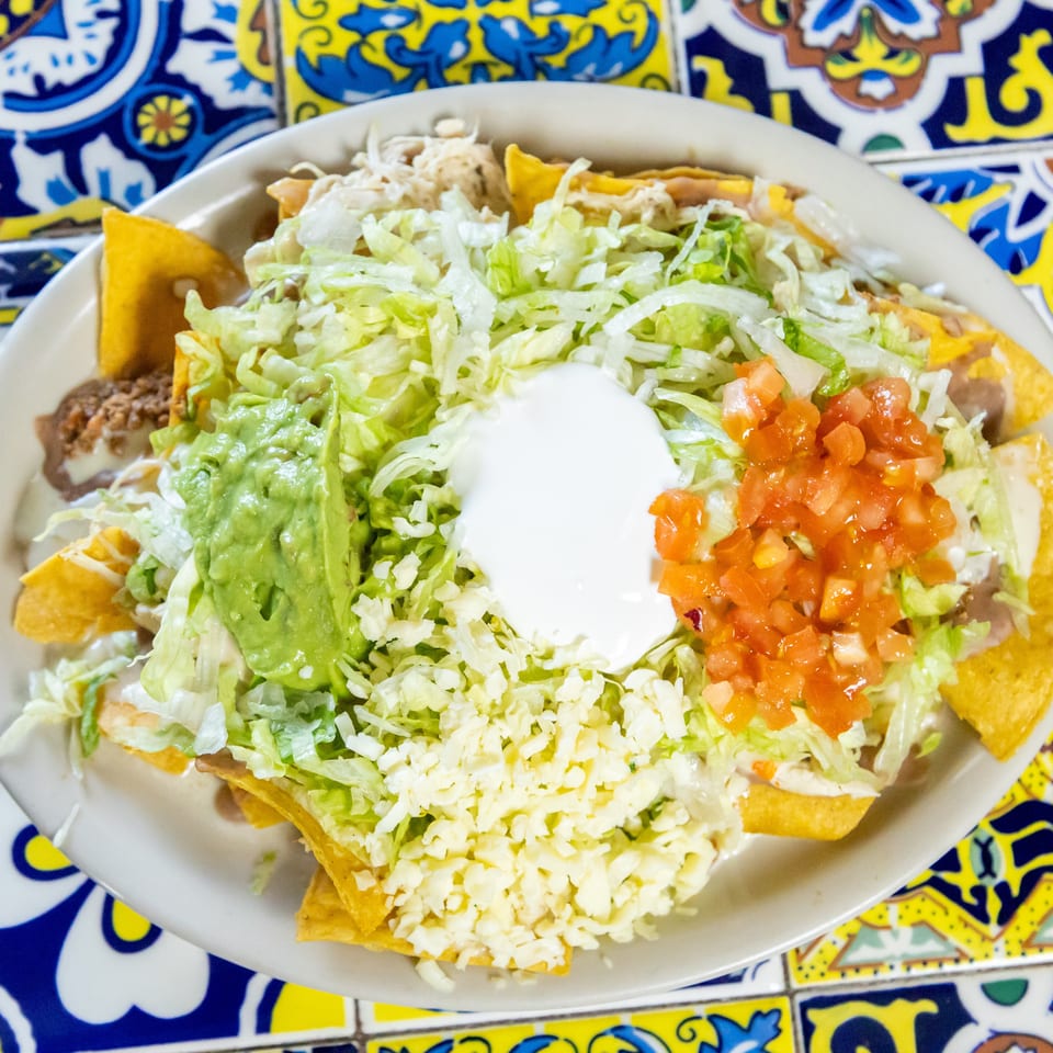 A plate of nachos with shredded lettuce, guacamole, sour cream, pico de gallo, and cheese.