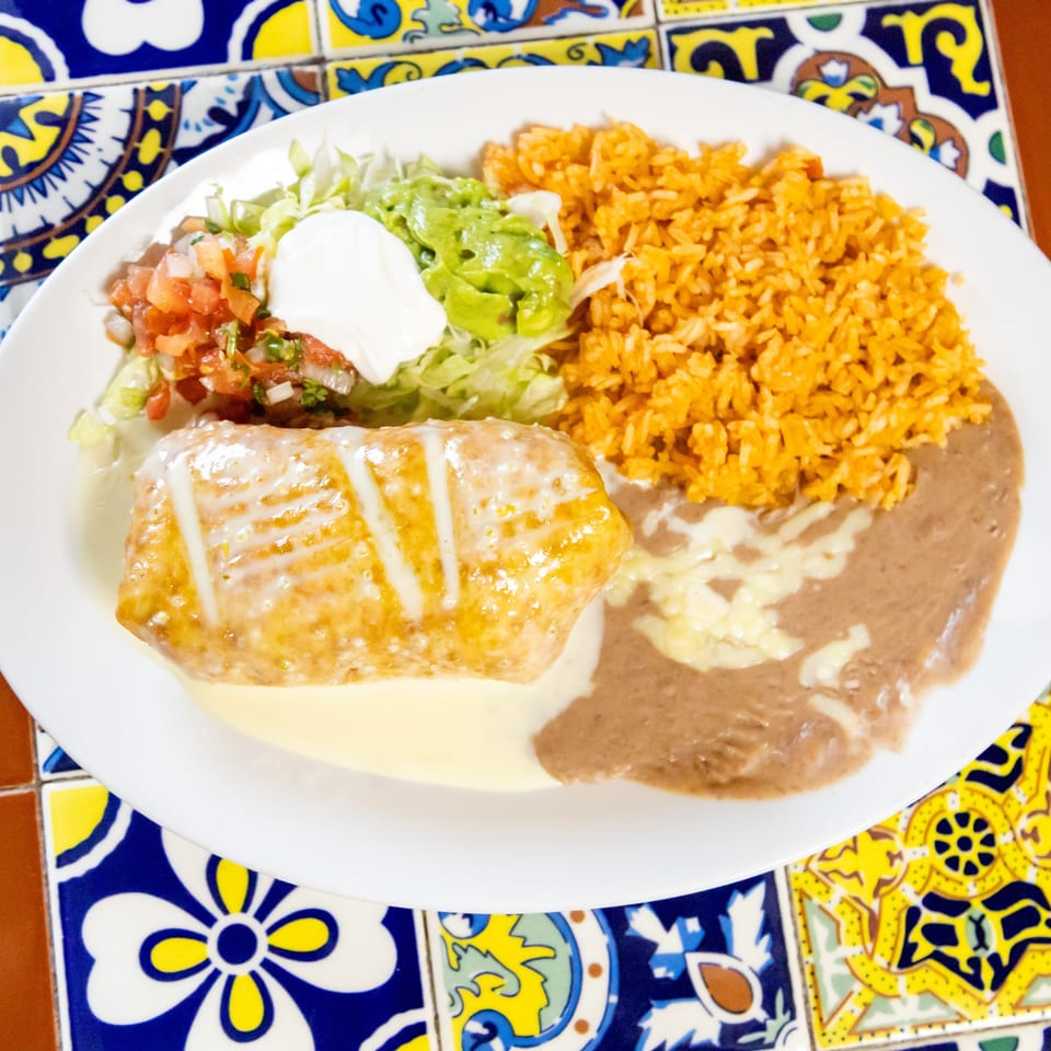 A Mexican combination plate with a chimichanga, rice, refried beans, guacamole, pico de gallo, and sour cream.