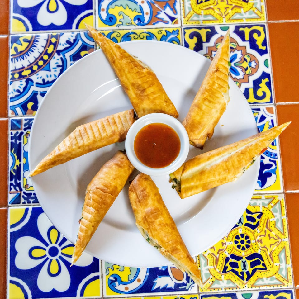 Golden-brown, triangular pastries arranged in a circle around a small dish of dipping sauce on a white plate.