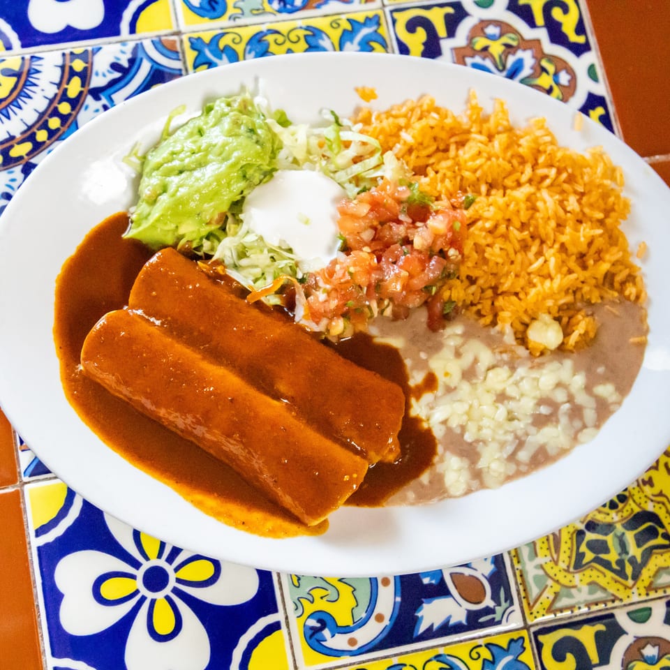 Two enchiladas with red sauce, rice, refried beans, guacamole, sour cream, and pico de gallo.